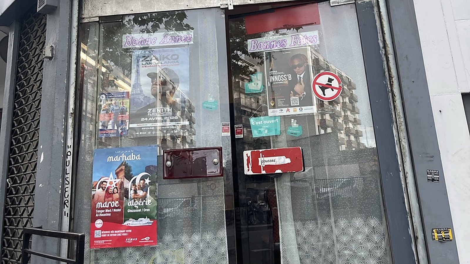 Affiche A3 d'une campagne collée côté rue sur la porte vitrée d'un restaurant à Aubervilliers, à côté d'autres affiches