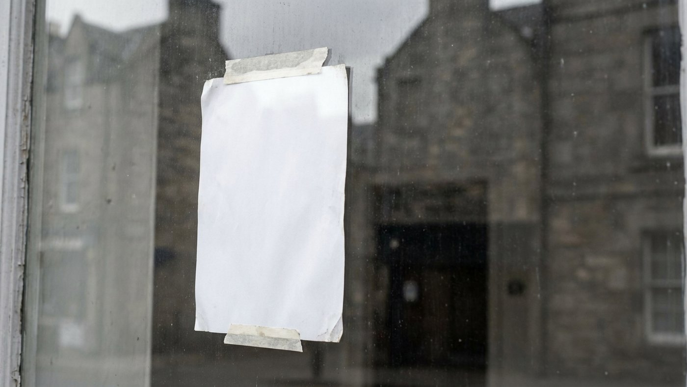 Gros plan d'une feuille blanche vierge fixée derrière la vitre d'une devanture de commerce, reflets d'une façade en pierre sur le verre