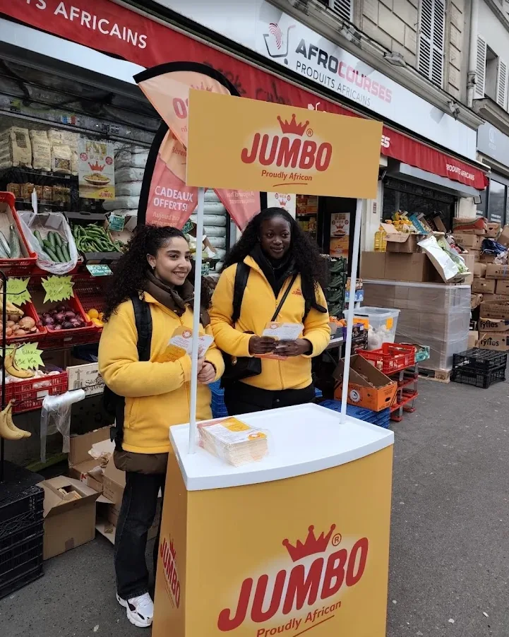 Deux animatrices Strevoo en tenue Jumbo tenant des flyers derrière un stand Jumbo installé devant une épicerie à Paris