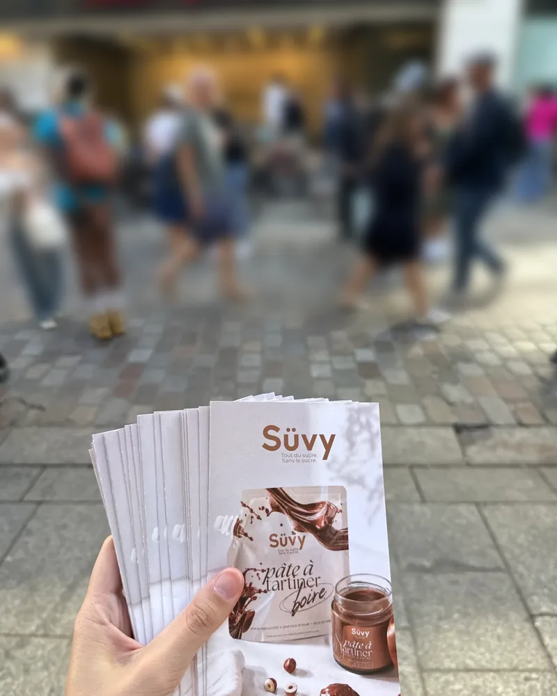 Flyers Süvy tenus en main pendant une distribution rue de Caumartin à Paris, passants en arrière-plan
