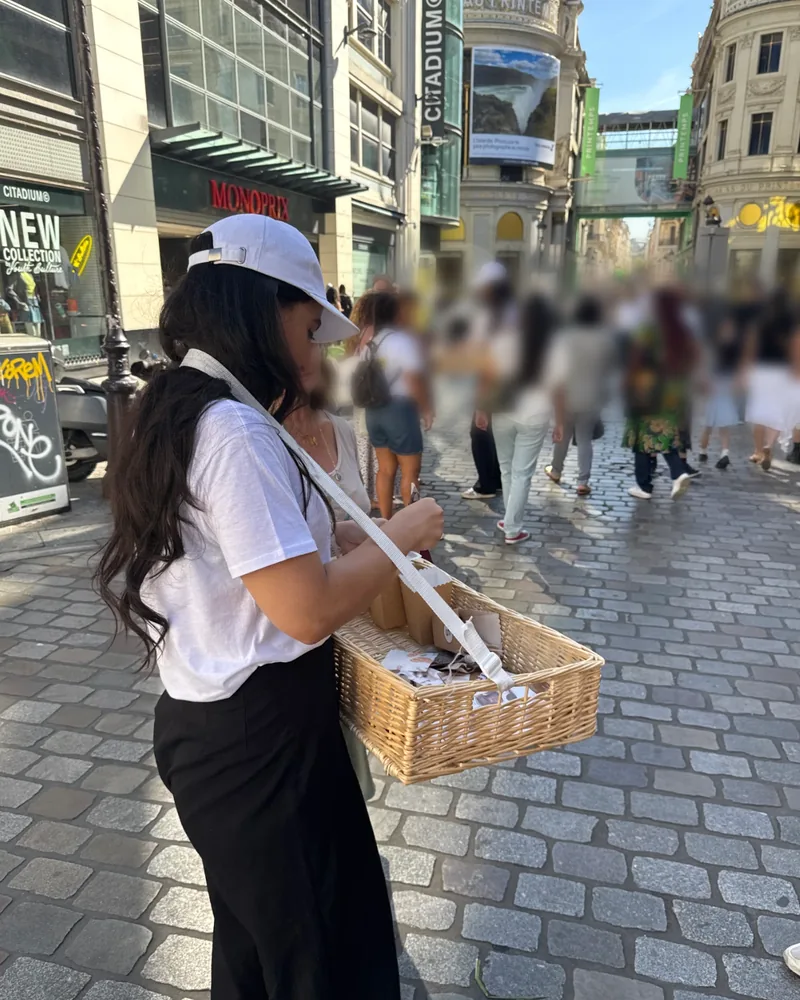 Animatrice Strevoo en casquette blanche distribuant les supports Süvy depuis un panier en osier, devant Citadium et le Printemps à Paris